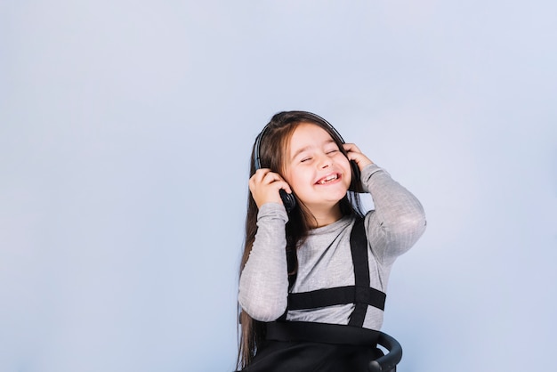 Smiling portrait of a girl enjoying the music on headphone against blue background