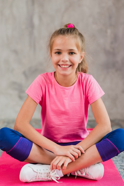 Free Photo smiling portrait of a girl sitting on pink carpet against grey concrete wall