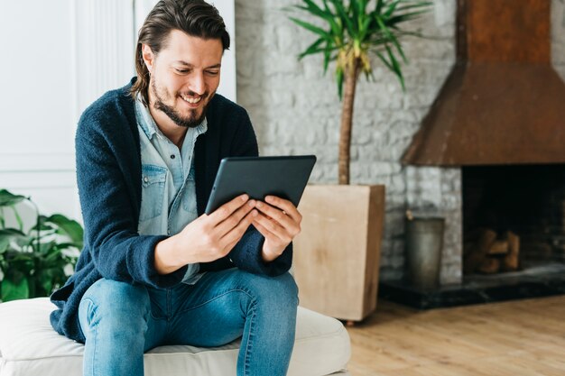 Smiling portrait of a handsome man sitting on couch looking at digital tablet