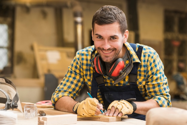 Free photo smiling portrait of a male carpenter taking measurement with ruler and pencil on wooden block