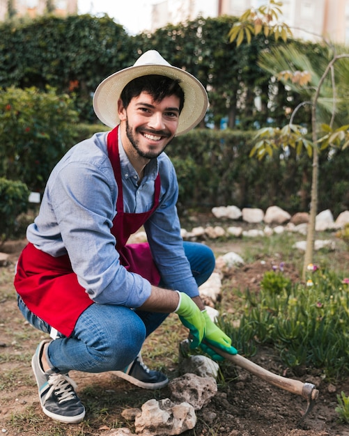 Free photo smiling portrait of a male gardener digging the soil with hoe in the vegetable garden