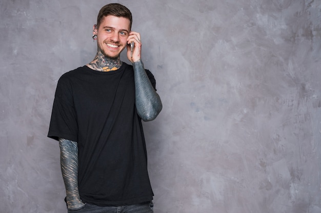 Smiling portrait of a tattooed young man with pierced ears talking on mobile phone