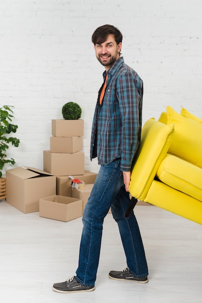 Free photo smiling portrait of a young man lifting the yellow sofa in new house