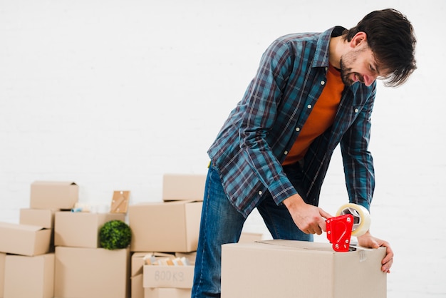 Smiling portrait of a young man sealing cardboard box with duct tape