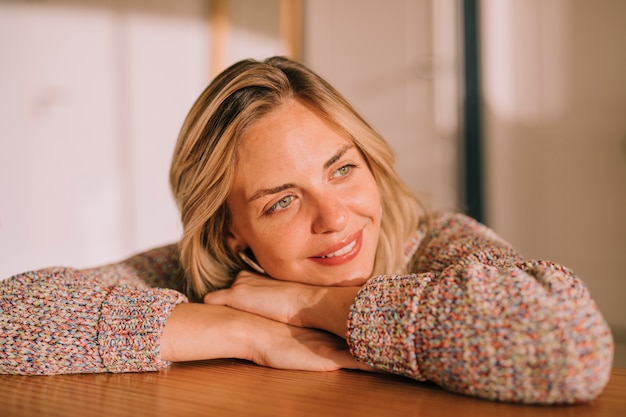 Smiling portrait of a young woman leaning on wooden desk daydreaming