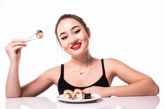 Free photo smiling pretty asian look with modest hairdo sit on the table eat sushi rolls smiling isolated on white