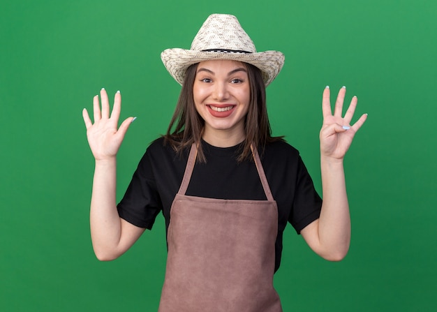 Smiling pretty caucasian female gardener wearing gardening hat gesturing nine with fingers on green