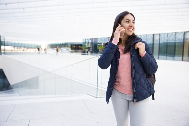 Smiling pretty girl with satchel using mobile phone outdoors