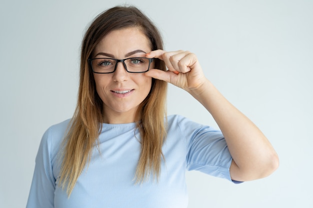 Smiling pretty lady adjusting glasses and looking at camera. 