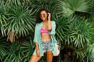 Free photo smiling pretty woman in stylish summer outfit posing over tropical  garden wearing  straw bag and   bracelets