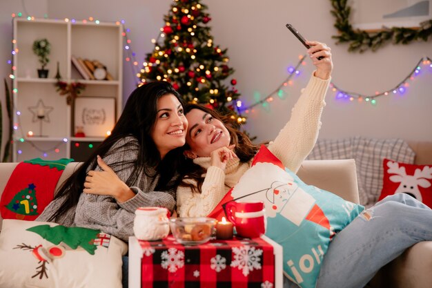 smiling pretty young girls take selfie sitting on armchairs and enjoying christmas time at home