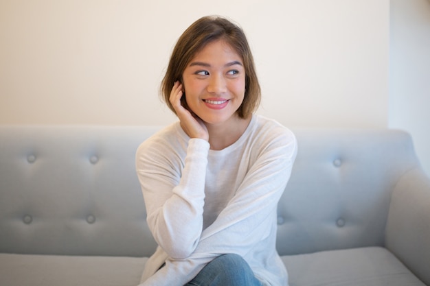 Free photo smiling pretty young woman relaxing and sitting on sofa at home