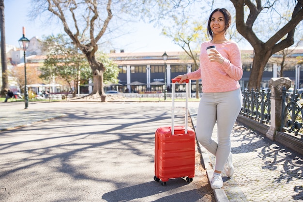 Smiling pretty young woman with trolley case outdoors