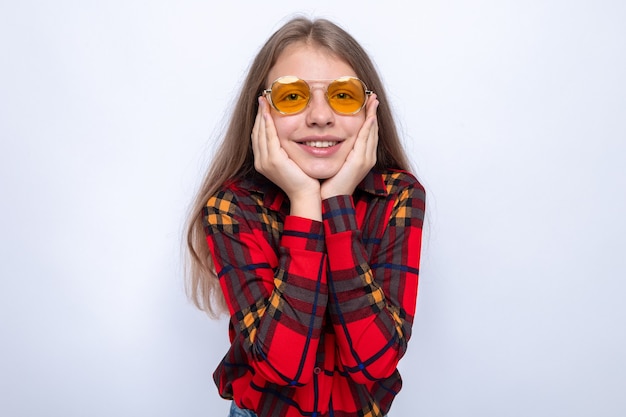 Smiling putting hands on cheeks beautiful little girl wearing red shirt and glasses isolated on white wall