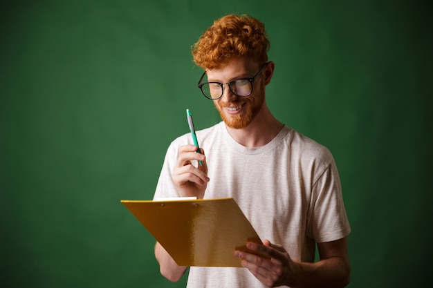 Free photo smiling readhead bearded man in white tshirt holding folder and pen