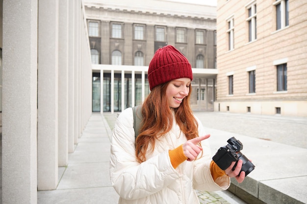 Smiling redhead girl photographer taking pictures in city makes photos outdoors on professional came