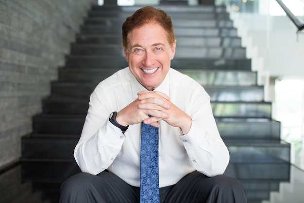 Free photo smiling senior businessman sitting on stairs