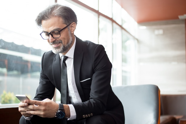 Free photo smiling senior man checking message on phone