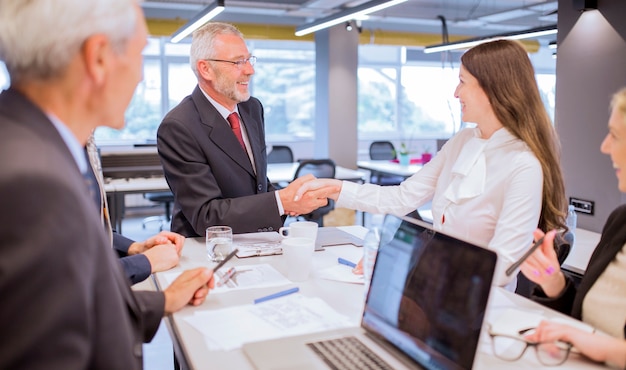 Smiling senior man shaking hands with young businesswoman in the office