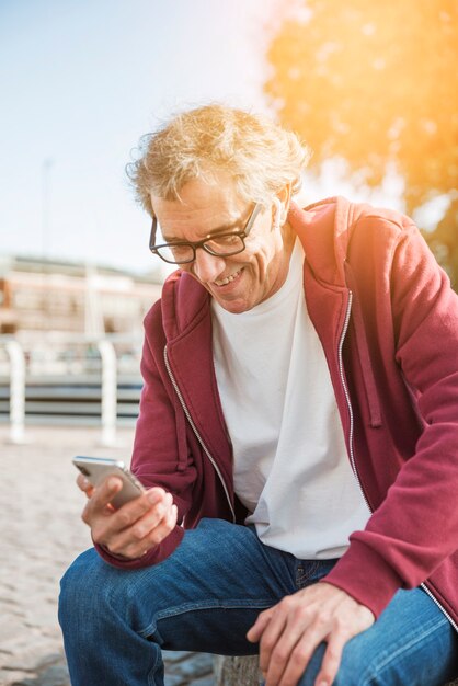 Smiling senior man sitting in park looking at smartphone