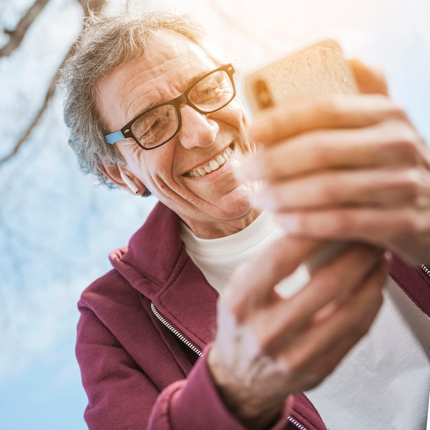 Free photo smiling senior man wearing eyeglasses using smart phone