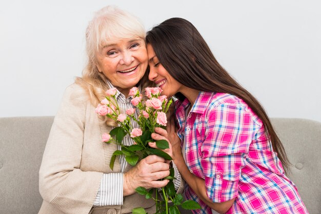 Smiling senior mother leaning her head on her senior mother's shoulder holding roses