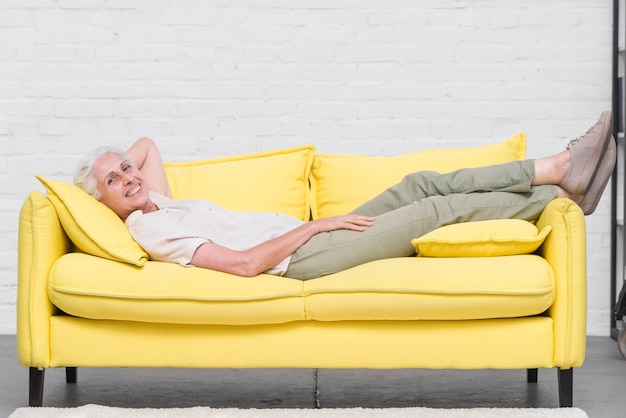 Free photo smiling senior woman relaxing on yellow sofa at home