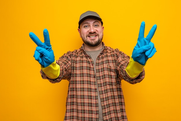 Smiling slavic cleaner man with rubber gloves gesturing victory sign 