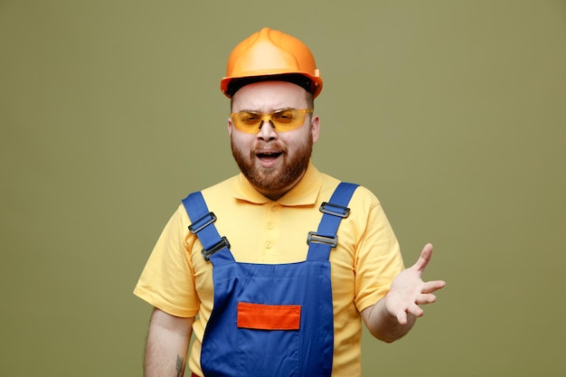 Free Photo smiling spreading hands young builder man in uniform isolated on green background