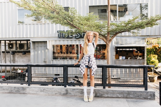 smiling tanned woman with blonde hair posing on street background.