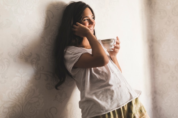 Smiling teenage girl leaning on wallpaper holding coffee cup