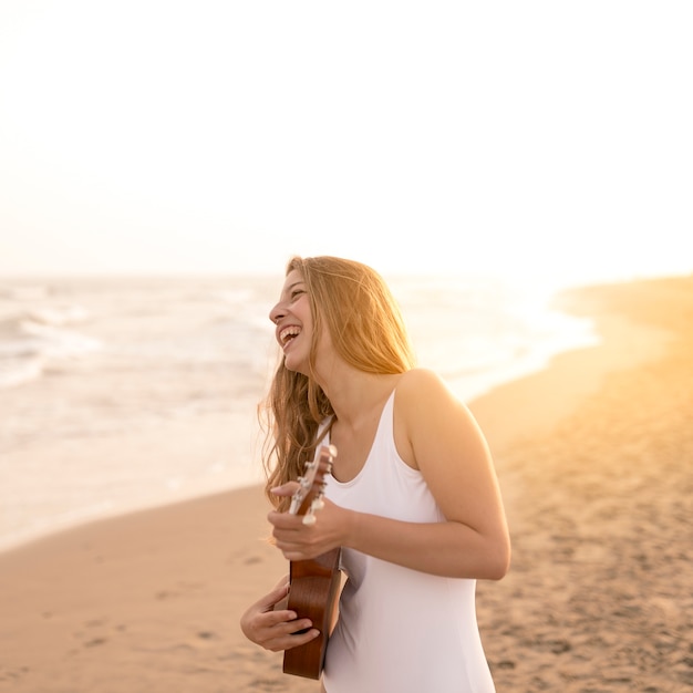 Free photo smiling teenage girl playing ukulele at beach