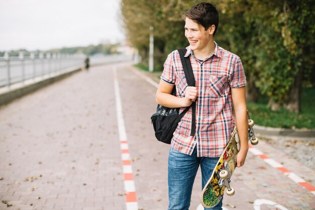 Smiling teenager carrying colorful skateboard