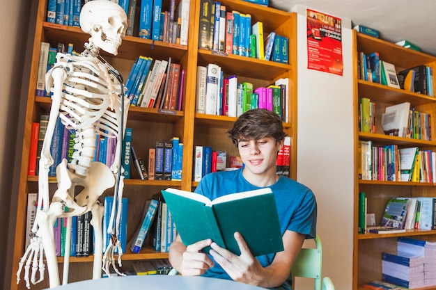 Free photo smiling teenager reading book at library table