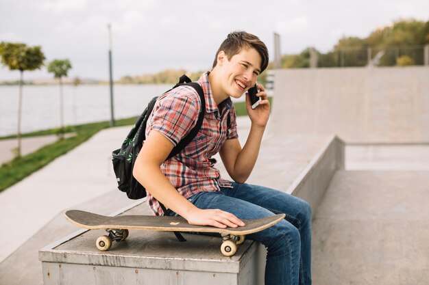 Smiling teenager talking on phone near skateboard