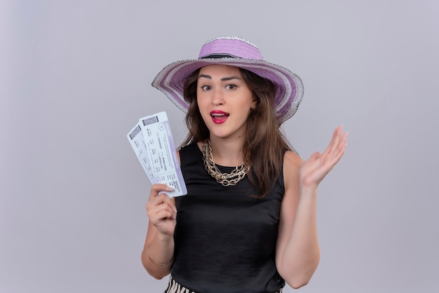 Smiling traveler young girl wearing black undershirt in hat holding tickets on white background