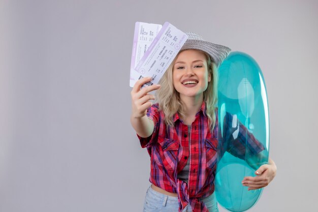 Smiling traveler young girl wearing red shirt in hat holding inflatable ring and tickets on isolated white background