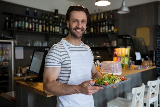 Free Photo smiling waiter carrying a tray of salad in restaurant