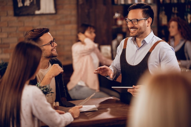 Free Photo smiling waiter holding digital tablet while taking order from a couple in a bar