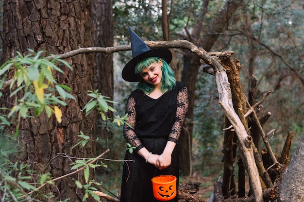 Free photo smiling witch woman in woods with pumpkin