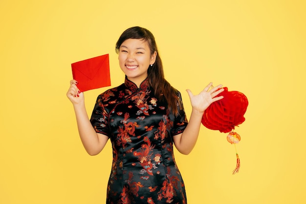 Free photo smiling with lantern and envelope. happy chinese new year 2020. asian young girl's portrait on yellow background. female model in traditional clothes looks happy.  copyspace.