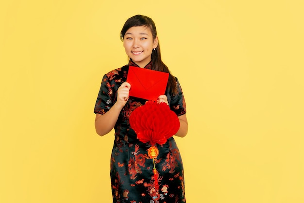 Free Photo smiling with lantern and envelope. happy chinese new year 2020. asian young girl's portrait on yellow background. female model in traditional clothes looks happy.  copyspace.