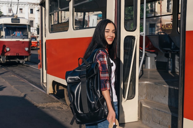 Free photo smiling woman carrying backpack standing near tram on street