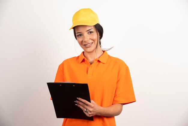 Smiling woman courier holding clipboard on white wall.