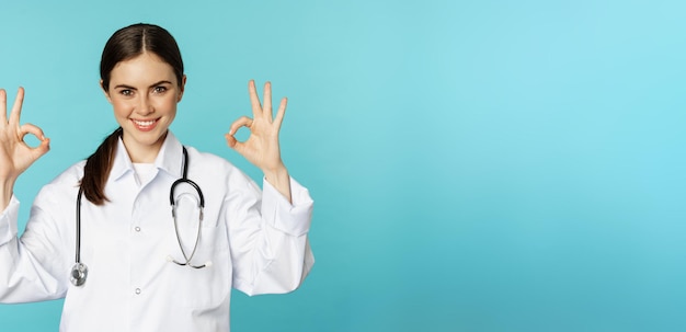 Free Photo smiling woman doctor professional medical worker showing okay ok sign in approval recommending clinic quarantine campaign torquoise background