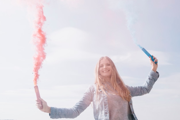 Smiling woman holding colored smoke bombs