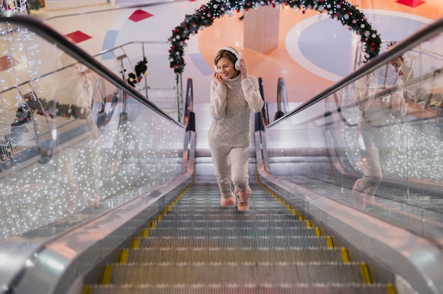 Free photo smiling woman holding headphones on head on escalator