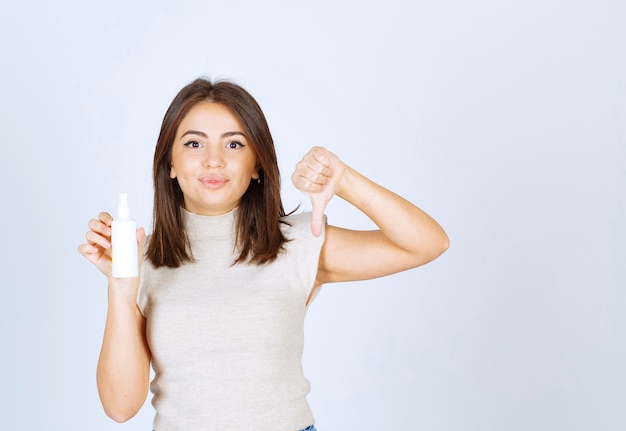 Smiling woman holding a spray and showing a thumb down .