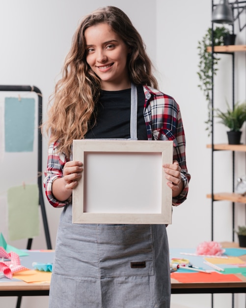 Smiling woman holding white empty picture frame looking at camera