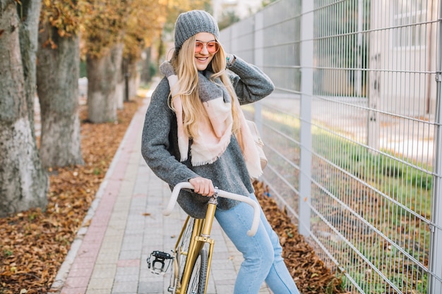 Smiling woman leaning on bicycle near fence